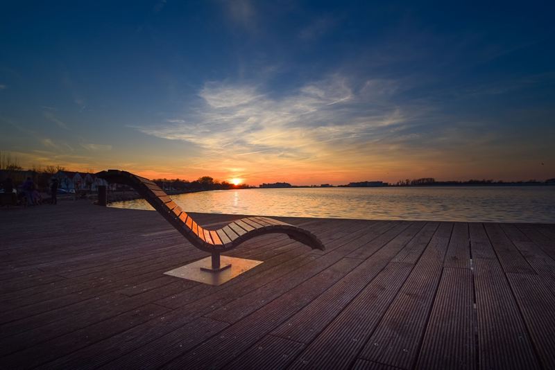 Sonnenuntergang über dem Wasser mit Sonnenliege auf Holzdeck
